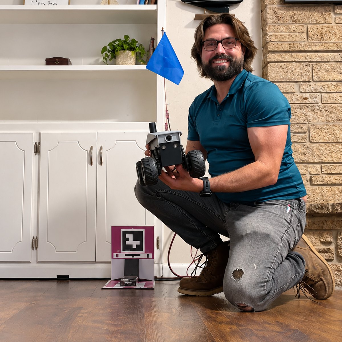 Landon "Cap" Whitt kneeling with the OKCREAL rover in his hands, its charging dock on the floor beside him